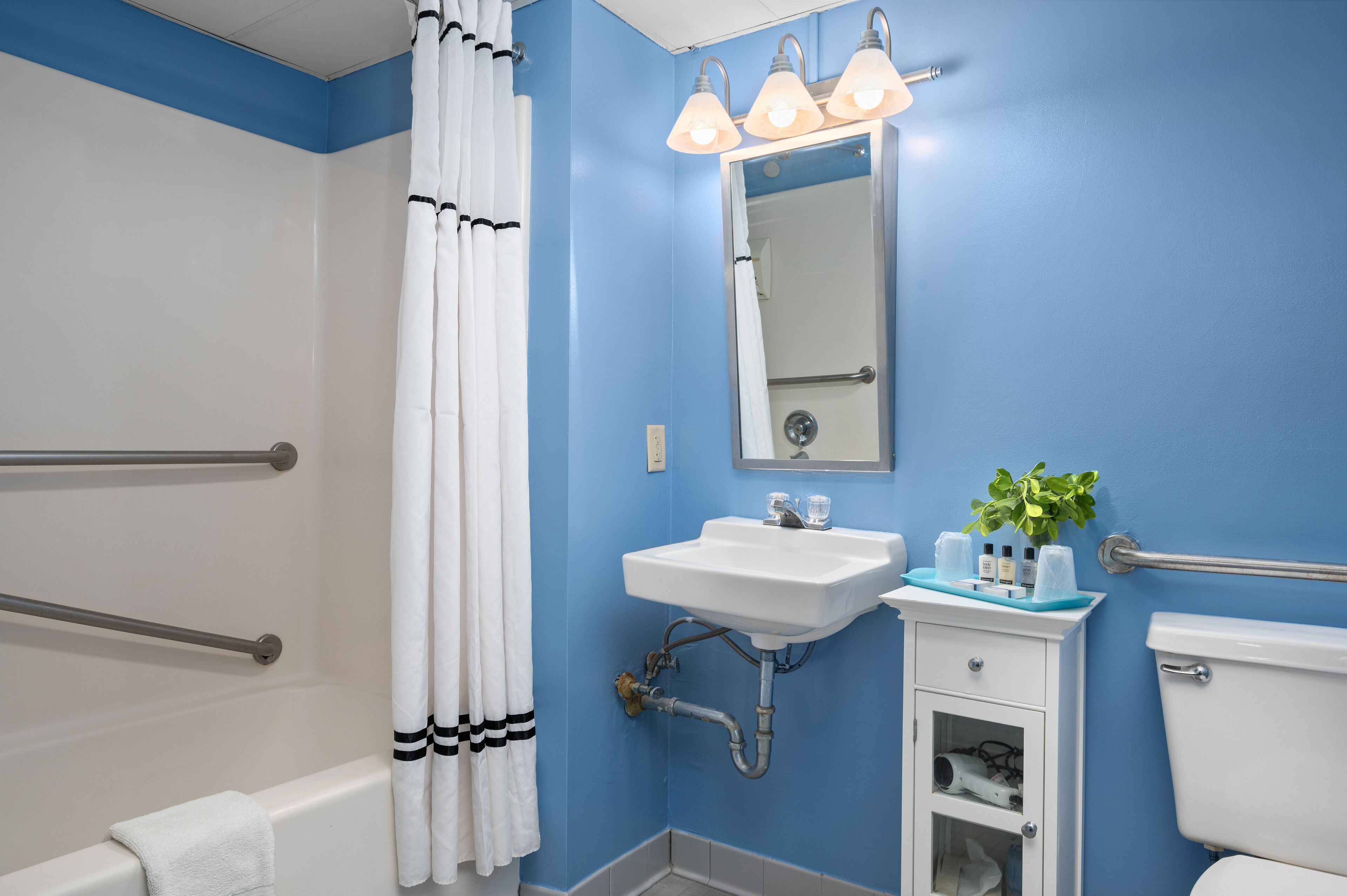 Une salle de bain avec un mur bleu, un lavabo blanc et une douche avec un rideau blanc.