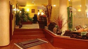 A hotel lobby with a wooden staircase, potted plants, and a reception desk. - Hotel Blue Rose's (Mesagne)