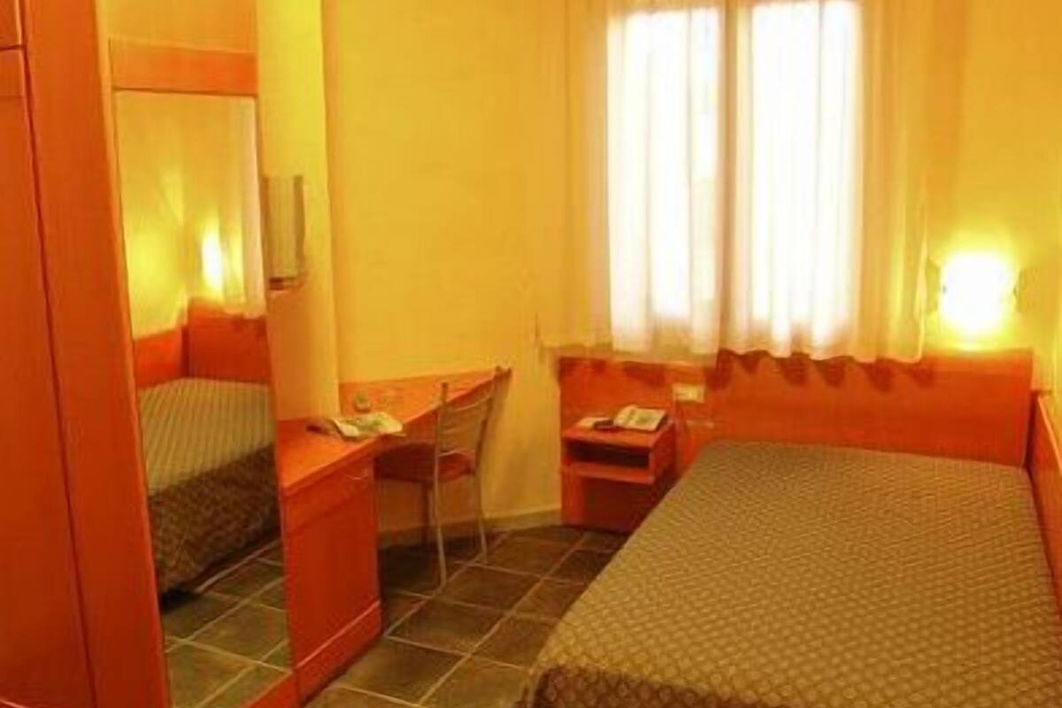 A hotel room with a bed, a desk, a chair, and a wardrobe.