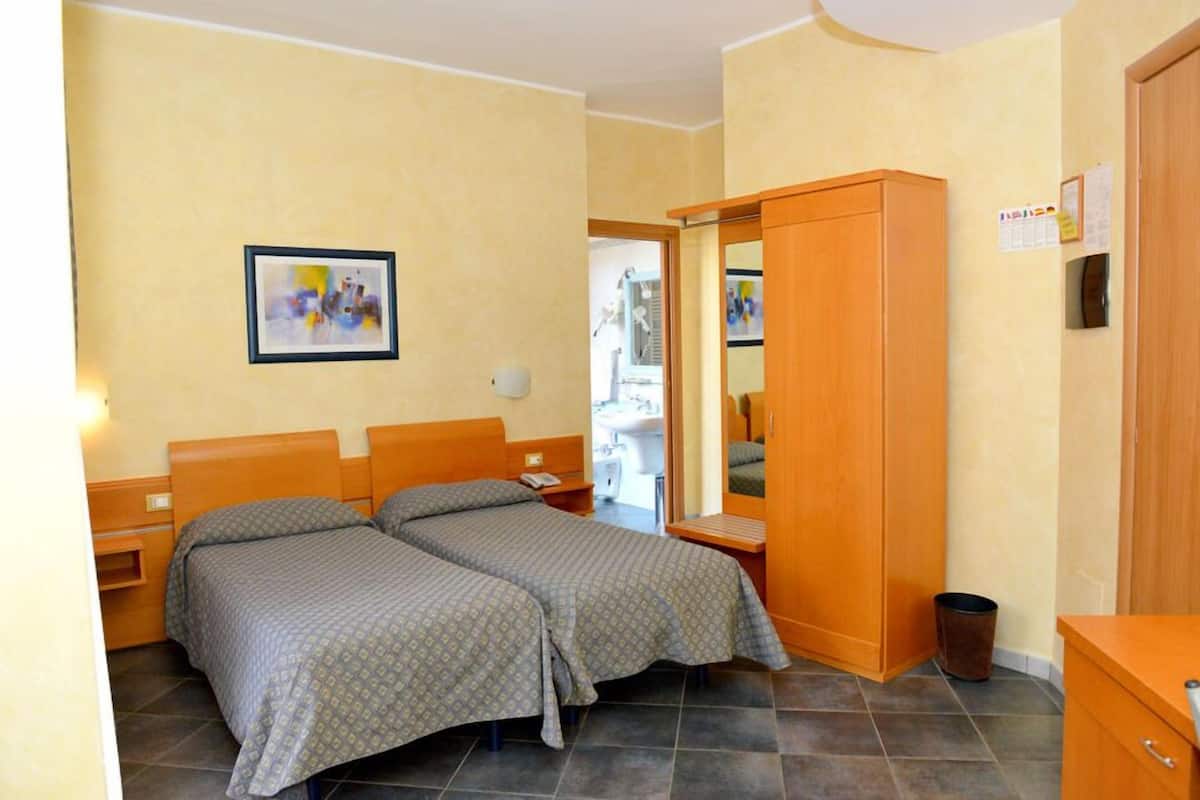 A room with two beds, a wooden wardrobe, a small table, and a wall-mounted picture.