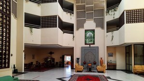 A spacious lobby with a high ceiling, a central seating area with two yellow armchairs, a red and black patterned rug, and a large wall-mounted artwork. - Hôtel Farah Safi (Safi)