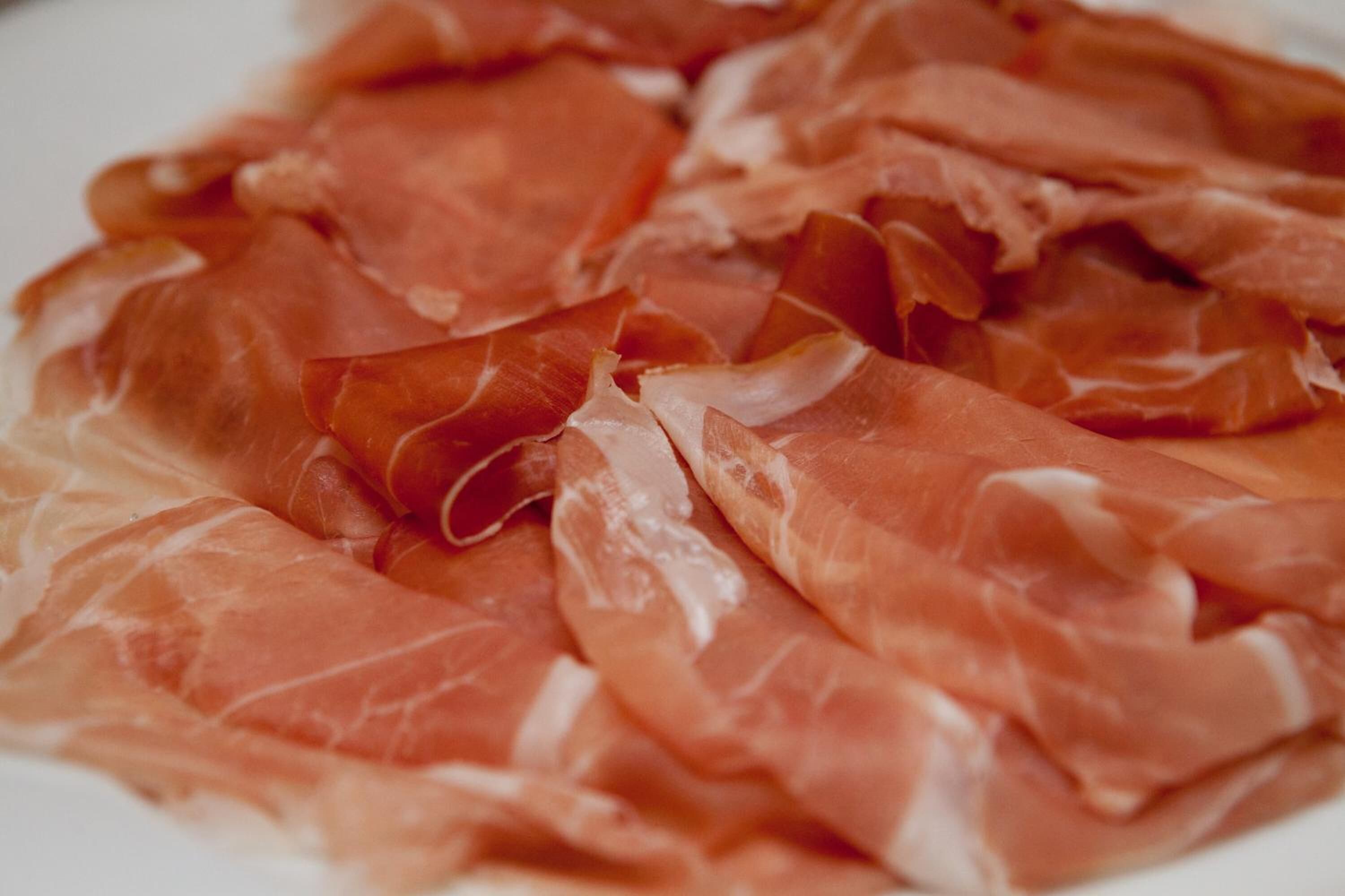 A plate of thinly sliced cured meat, likely prosciutto, arranged on a white plate.