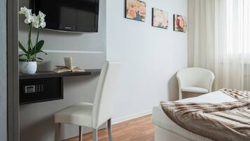 Ein modernes Hotelzimmer mit einem Bett, einem Schreibtisch mit Stuhl, einem an der Wand befestigten Fernseher und einem Fenster mit Vorhängen.