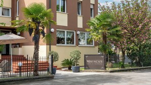A hotel entrance with a sign reading "Mini Palace Small & Charming," surrounded by palm trees and a fence. - Hotel Mini Palace Country House (Molinella)