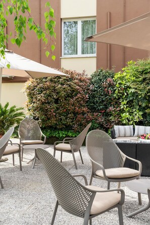 An outdoor seating area with wicker chairs and a sofa, surrounded by a hedge and a building with a window. - Hotel Mini Palace Country House (Molinella)