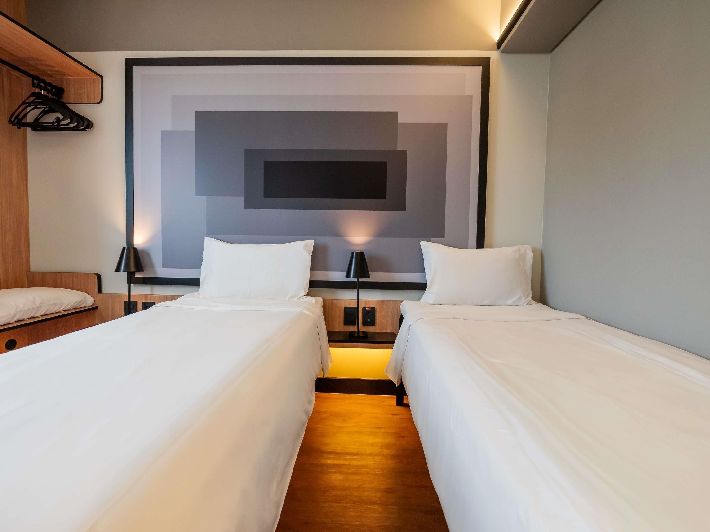 A hotel room with two beds, a large wall art piece, and a wooden headboard.