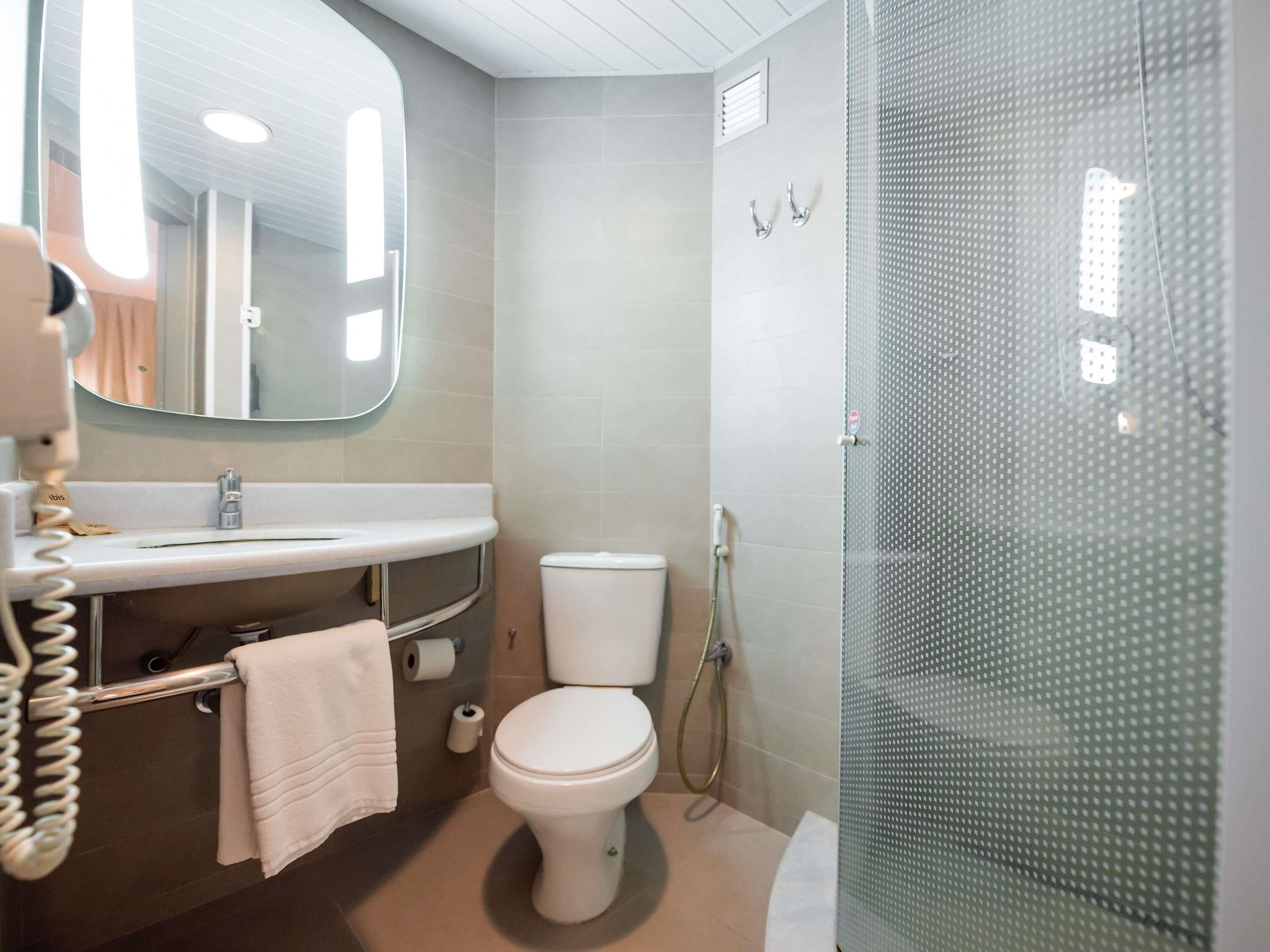 A bathroom with a toilet, sink, mirror, and shower enclosure.