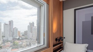 Habitación de hotel con un ventanal grande, paneles de madera, una cama y una lámpara de escritorio fijada a la pared.