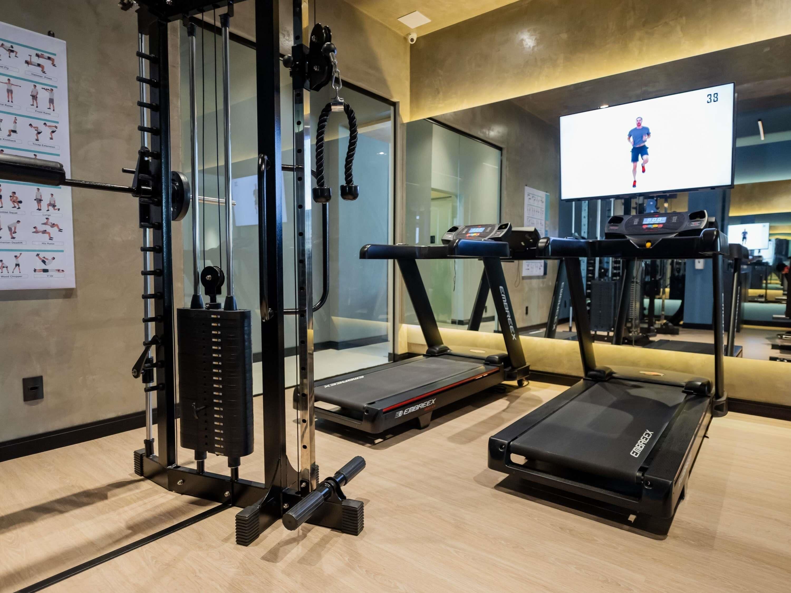 A gym with exercise equipment, treadmills, and a TV displaying a running person.