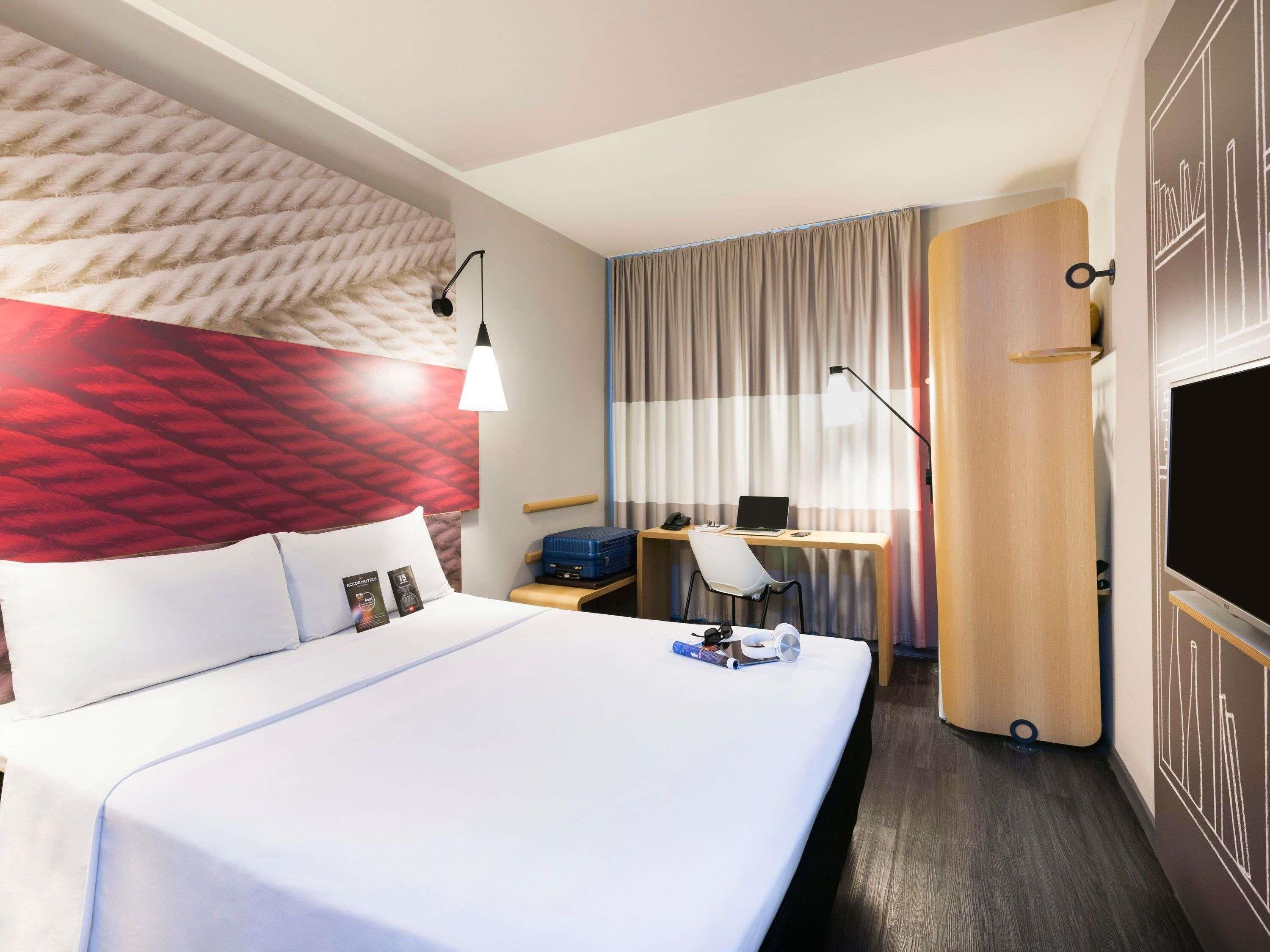 A hotel room with a bed, a desk with a laptop, a TV, and a door with a keyhole.