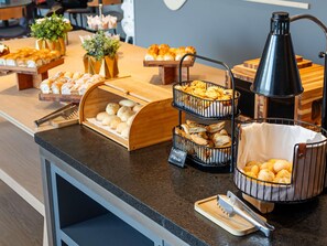 Un mostrador de buffet con diversas opciones de panadería, incluyendo pasteles y panes, dispuestos en pedestales de madera y cestas de alambre.