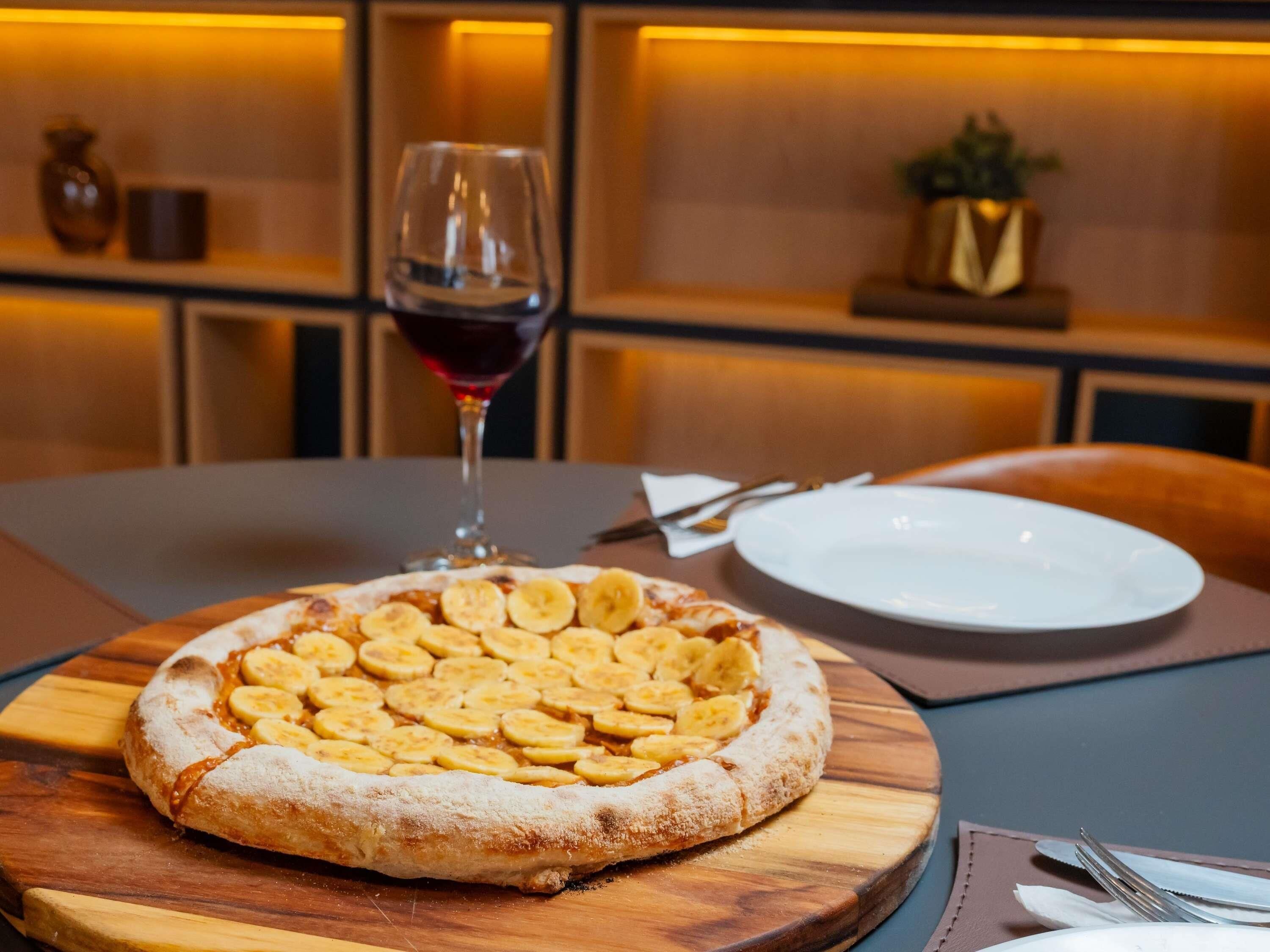 A pizza with banana slices on a wooden board on a table.