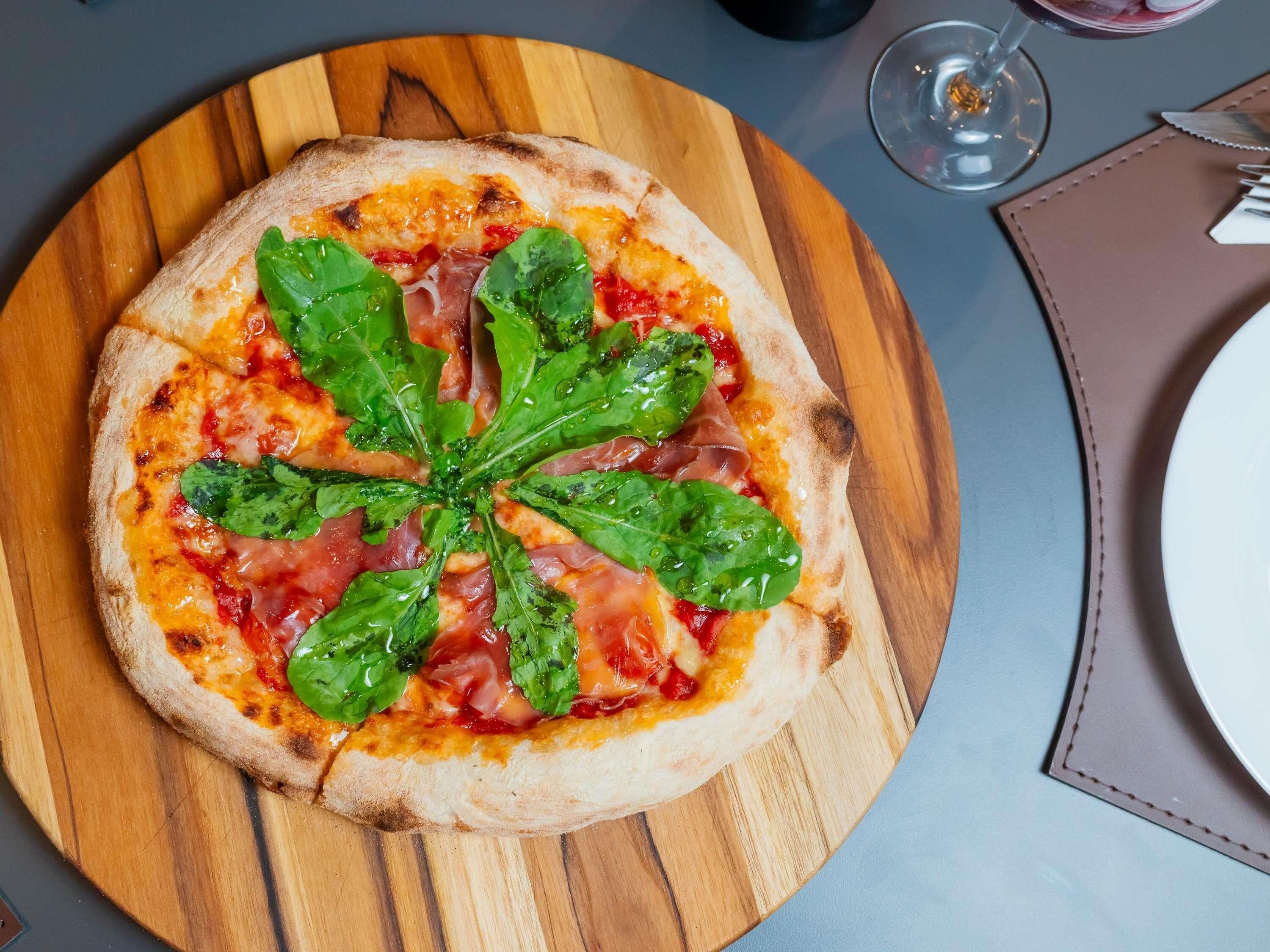 Une pizza aux épinards et au jambon de Parme, servie sur une planche en bois.