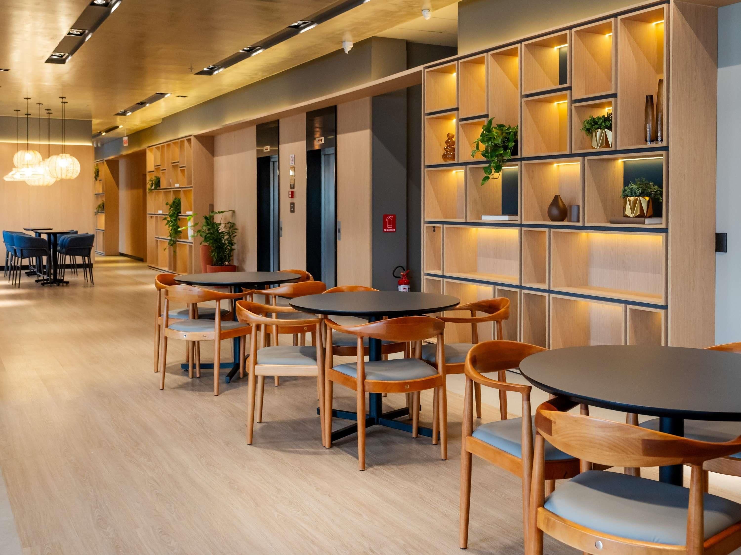 Un intérieur moderne avec des tables et des chaises rondes, des étagères en bois ornées de plantes et un détecteur d’incendie bien visible.