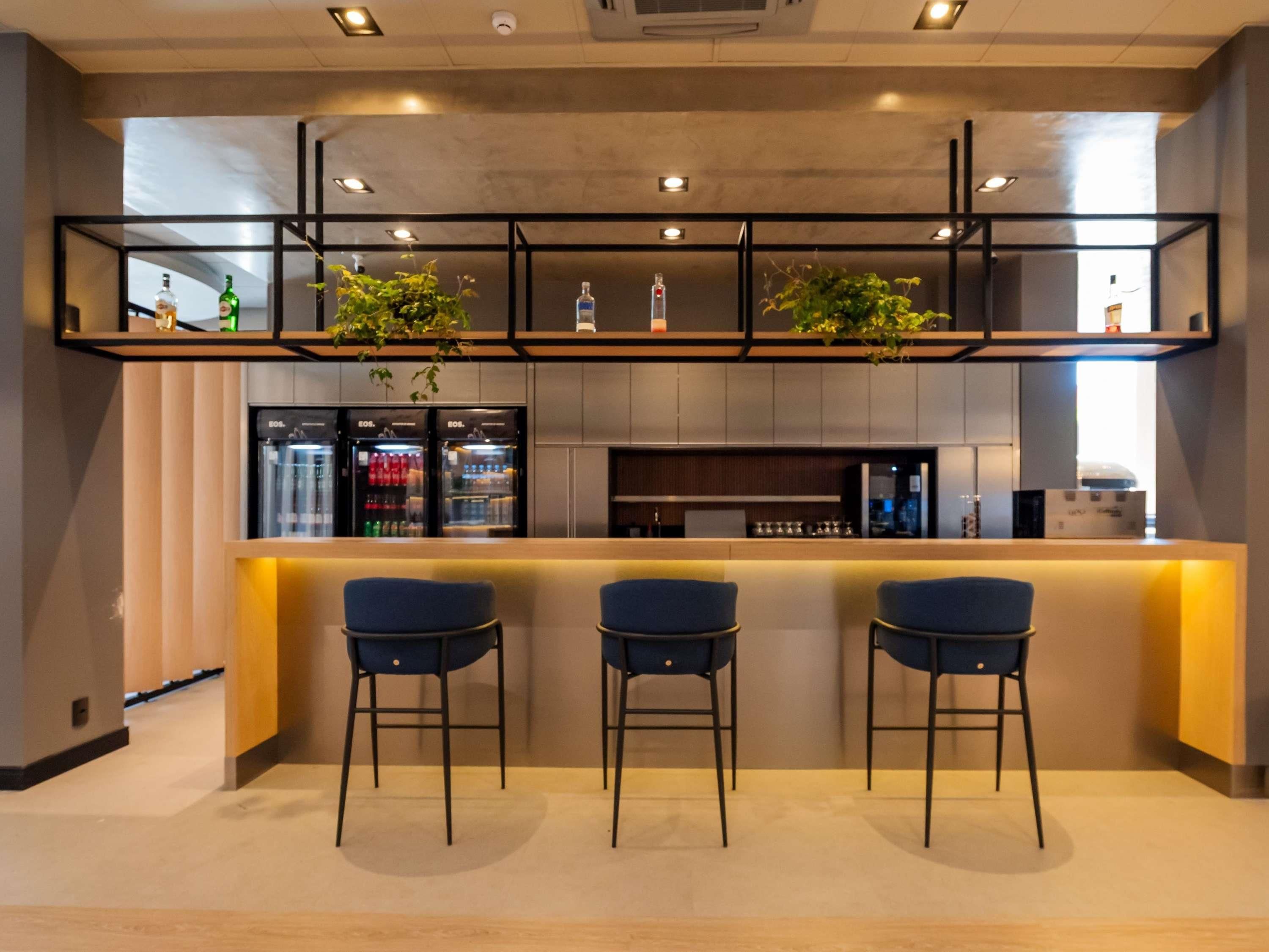 A modern kitchen with a bar area, three bar stools, and a refrigerator stocked with beverages.