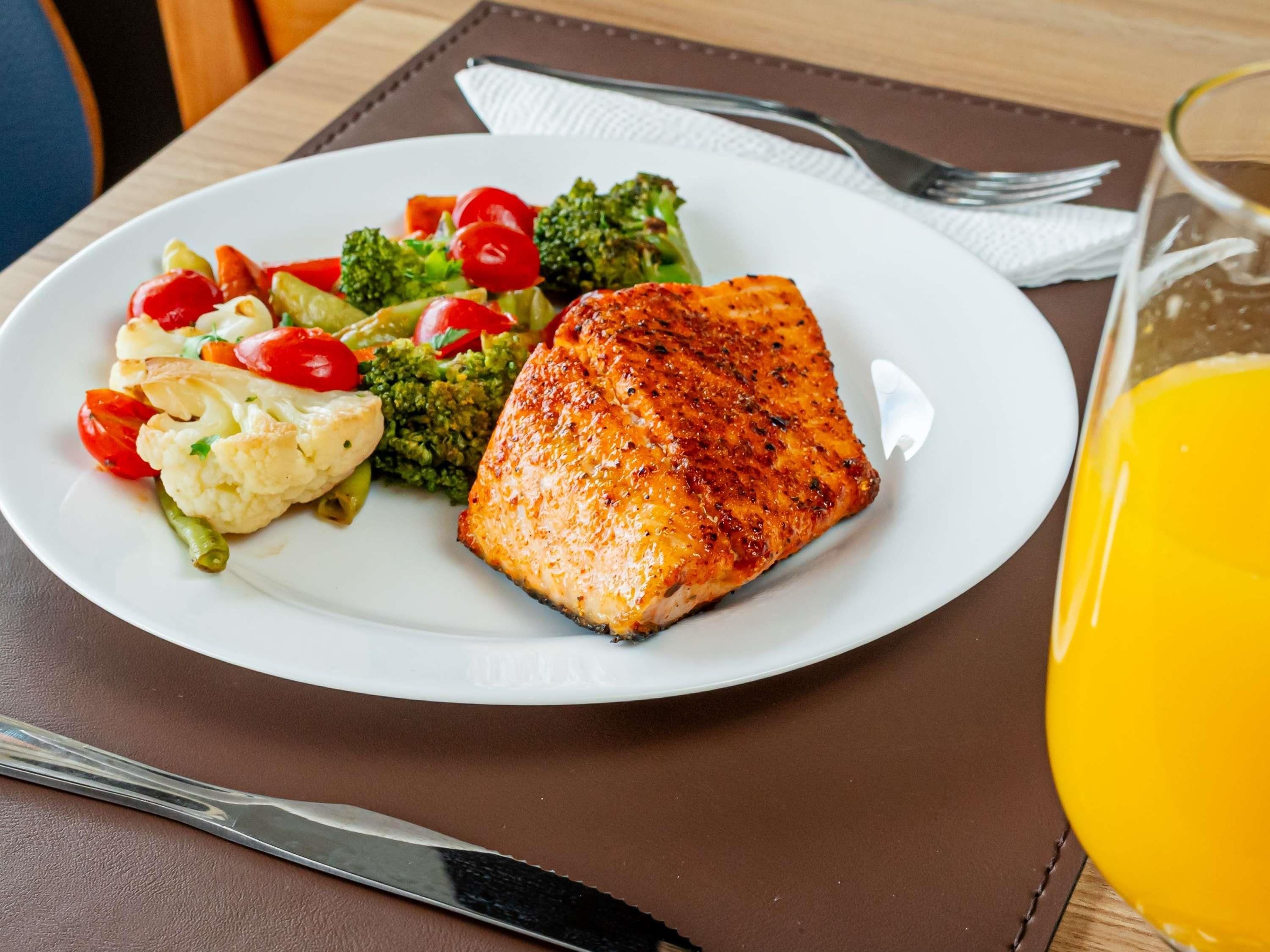 Prato com salmão grelhado, legumes cozidos no vapor e um copo de suco de laranja em uma mesa.