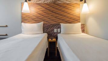 A hotel room with two beds, a headboard with a geometric pattern, and pendant lighting.