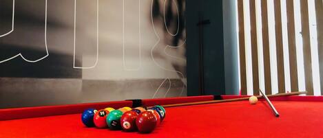 A red pool table with billiard balls in front of a wall with abstract designs.