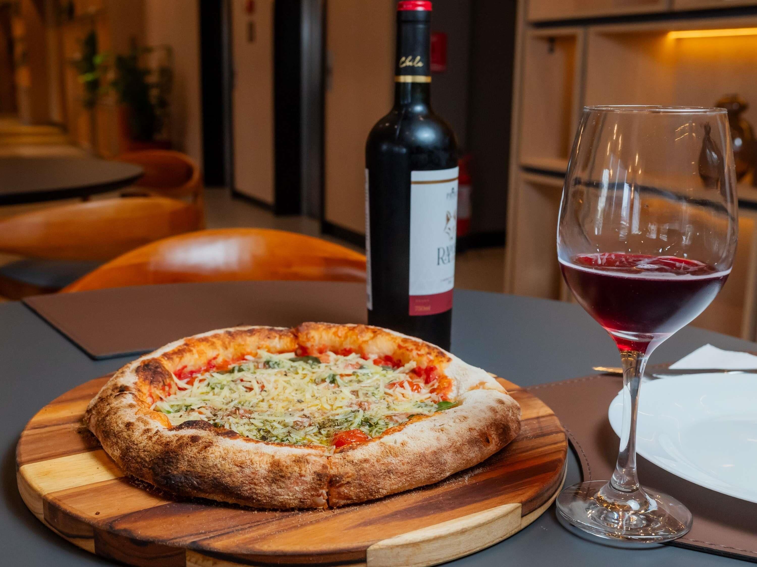 Eine Pizza auf einem Holzboden, eine Weinflasche und ein Weinglas auf einem Tisch.