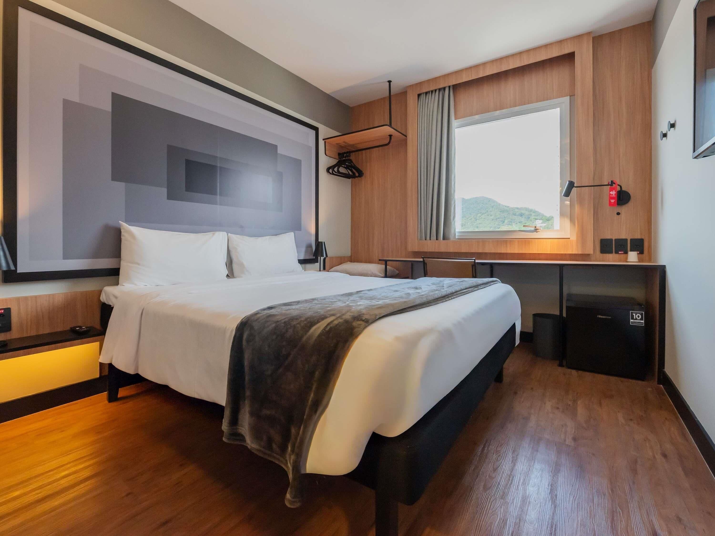 A modern hotel room with a large bed, a desk, and a window with a view of the outdoors.
