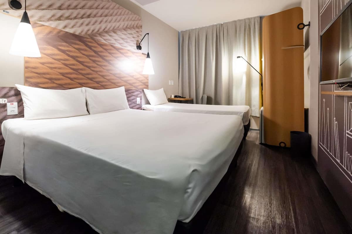 A hotel room with a large bed, two bedside tables, a desk, a chair, a TV, and a wardrobe.