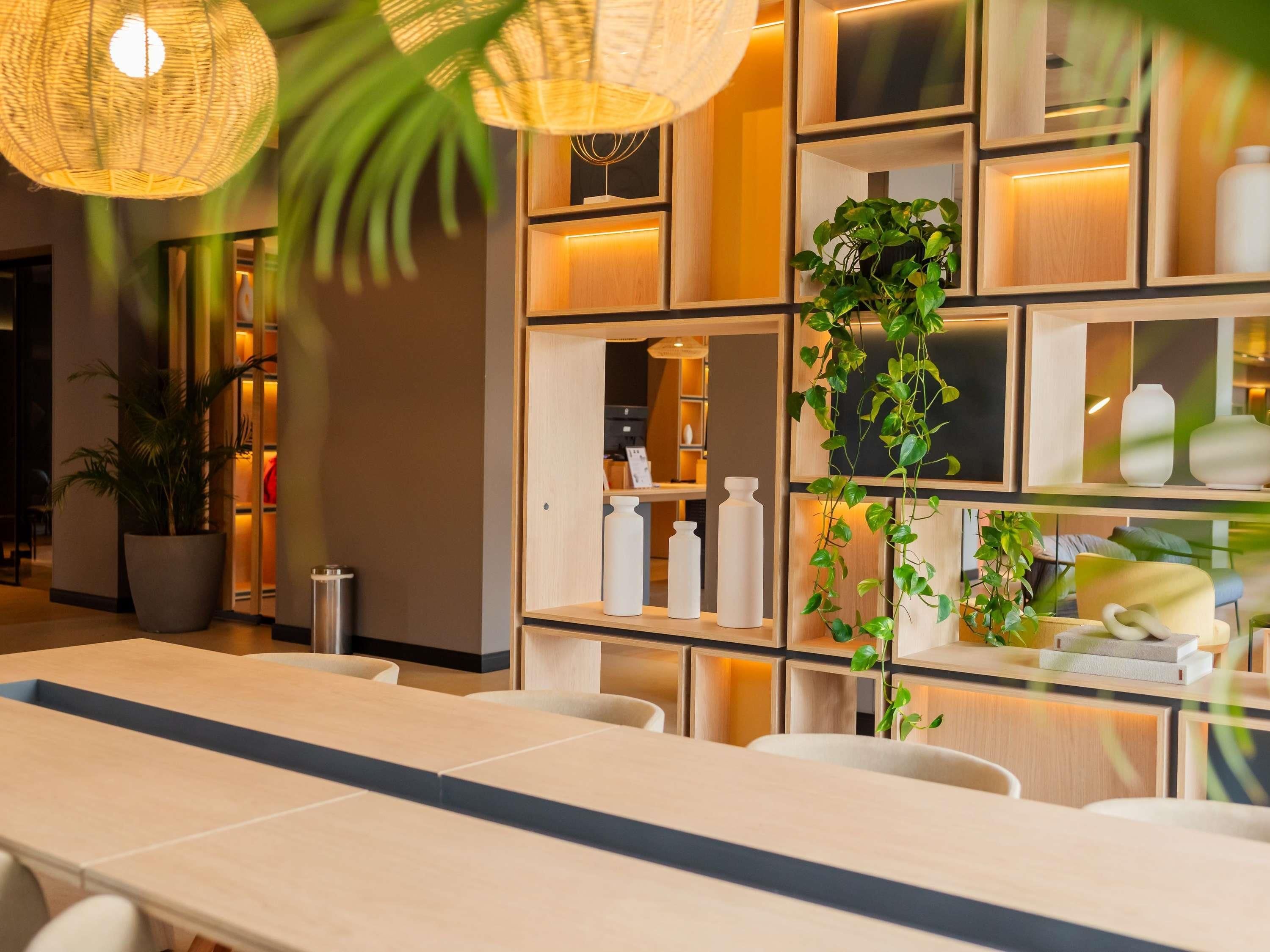 A modern interior with a long table, chairs, and a wall with shelves containing decorative items and plants.