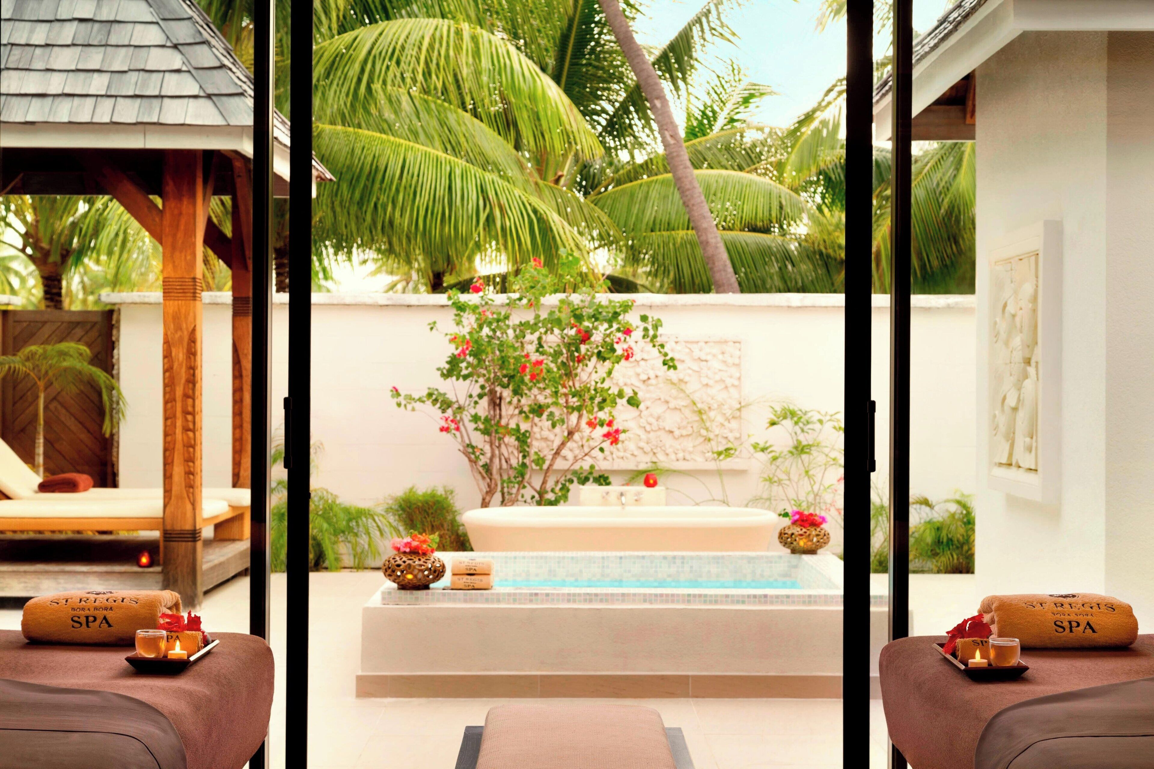 A spa area with two massage tables, a hot tub, and a view of palm trees.