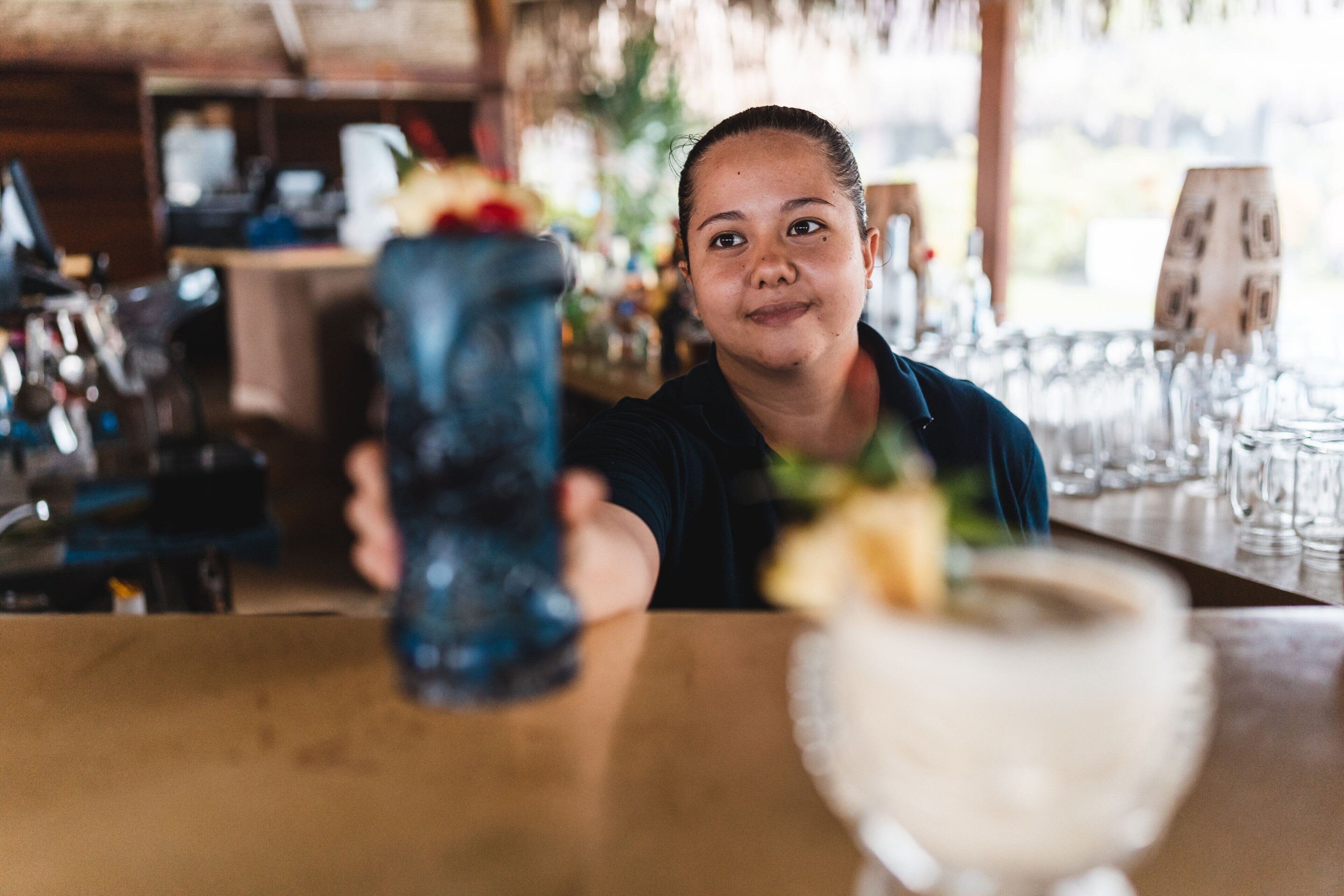 Une personne tient un verre bleu dans un bar, et un verre blanc est posé devant elle.