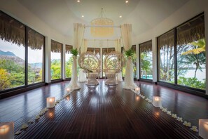 A spacious room with large windows, a wooden floor, and a central seating area with chairs and a decorative canopy.