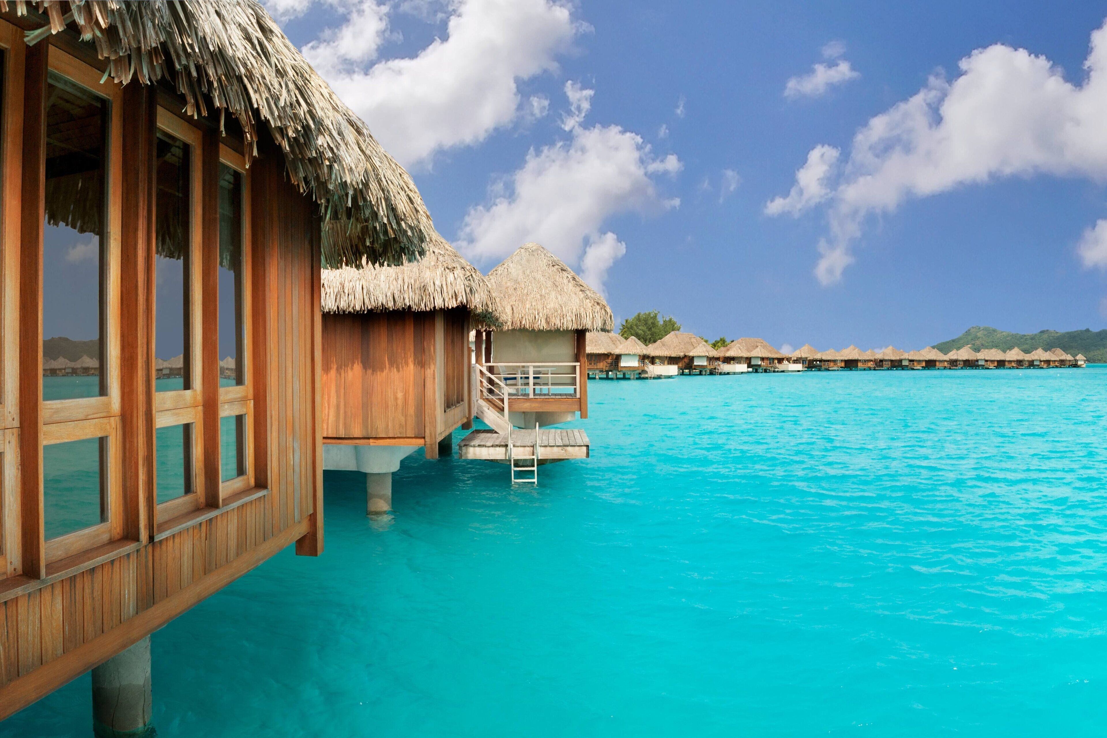 Cabañas sobre el agua con techos de paja, barandillas de madera y un mar azul cristalino.