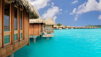Cabañas sobre el agua con techos de paja, barandillas de madera y un mar azul cristalino.
