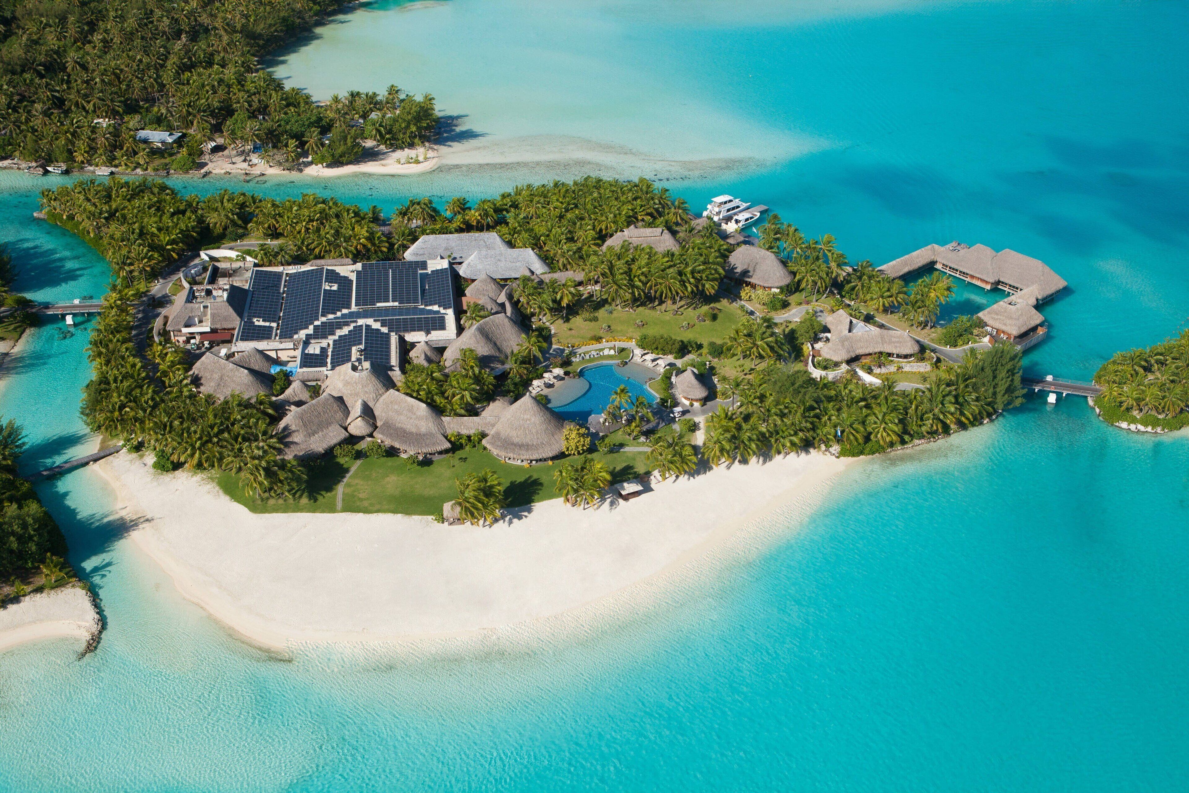 Vista aérea de un resort tropical con edificios de techo de paja, una piscina y abundante vegetación.