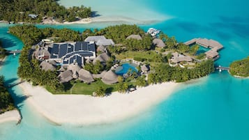 Vista aérea de un resort tropical con edificios de techo de paja, una piscina y abundante vegetación.