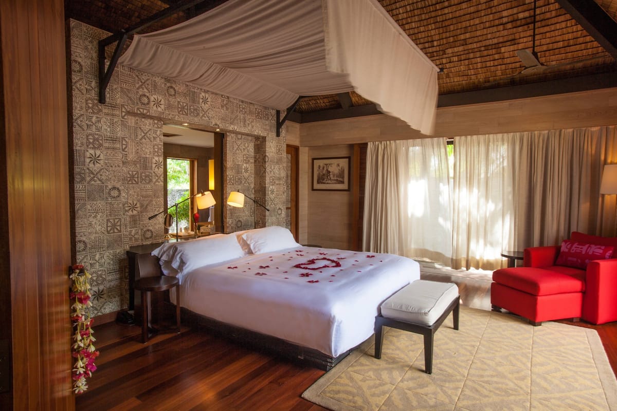 Quarto de hotel com uma cama grande, um sofá vermelho, uma mesa pequena e um painel decorativo.