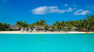 Un resort en la playa con cabañas de techo de paja, palmeras y aguas turquesas cristalinas.