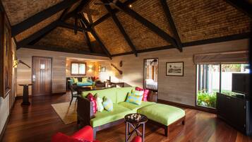 Een ruime woonkamer met een hoog houten plafond, een groene bank met kleurrijke kussens, een rode fauteuil en een houten salontafel.
