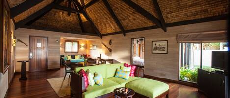 A spacious living area with a high wooden ceiling, a green sofa with colorful cushions, a red armchair, and a wooden coffee table.