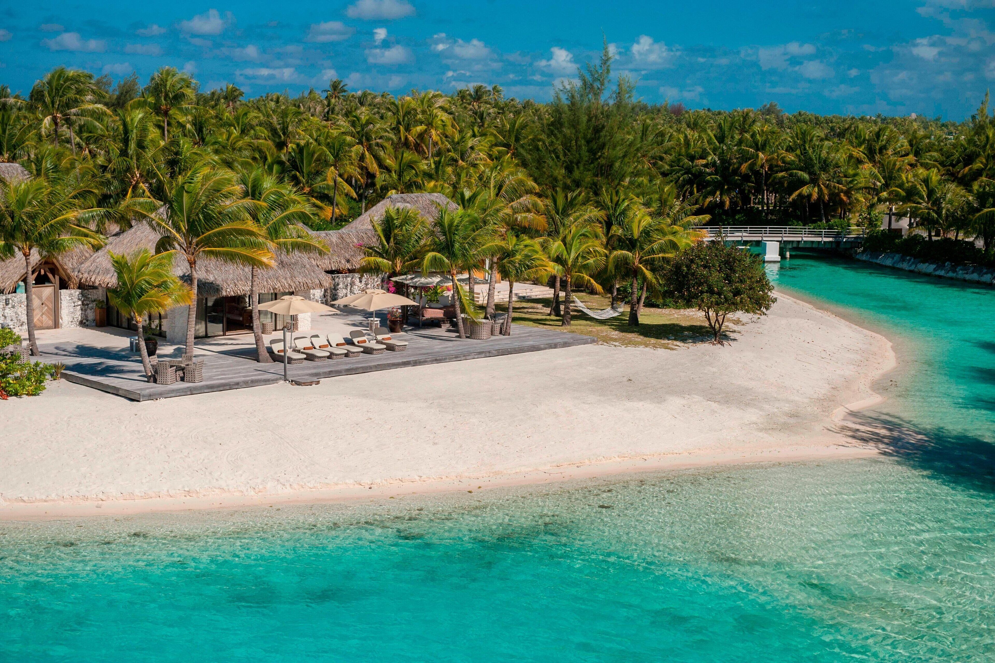 A beach resort with thatched-roof huts, palm trees, and a clear turquoise sea.