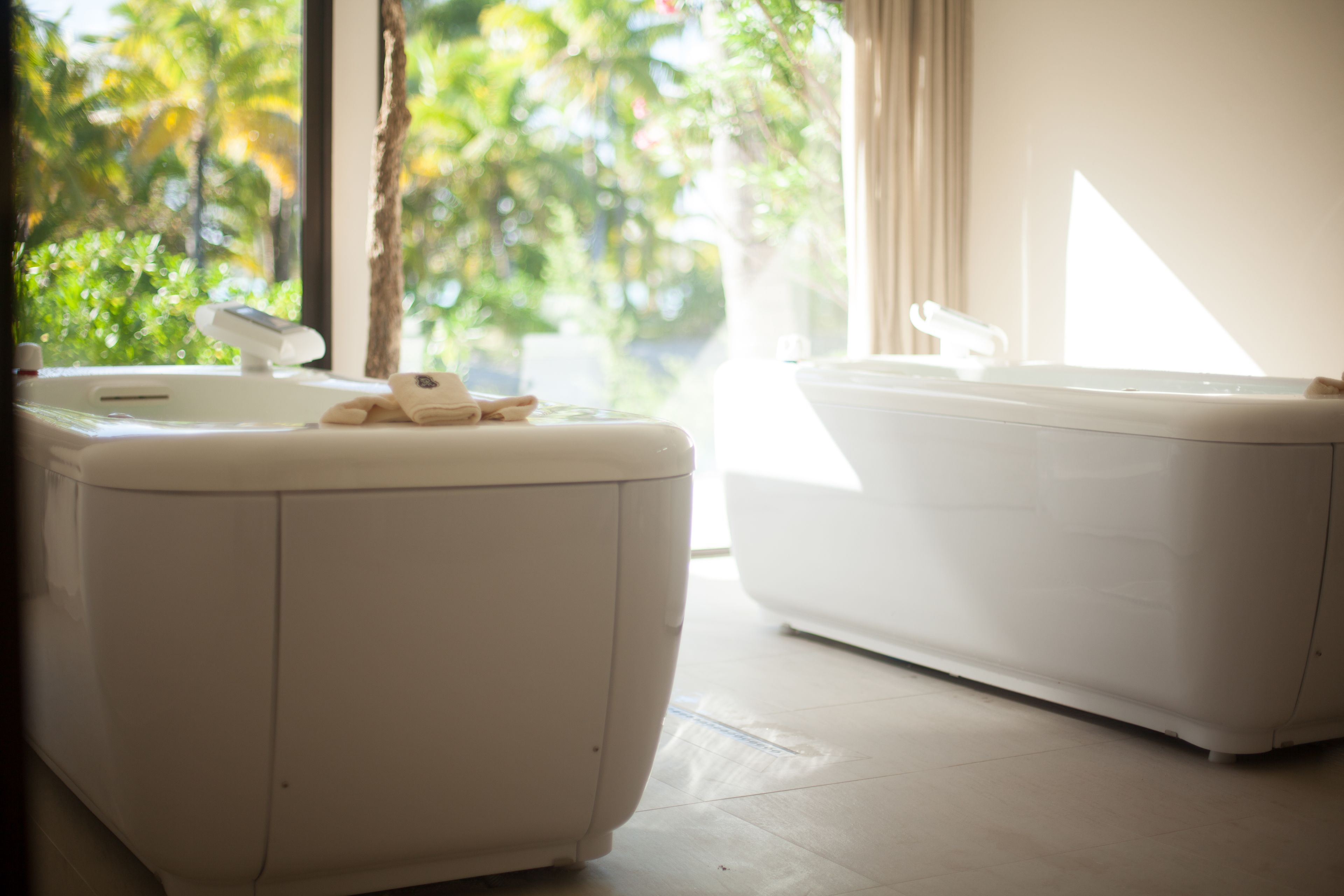 A bathroom with a white sink and bathtub, a towel on the sink, and a view of greenery outside.