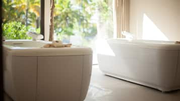 A bathroom with a white sink and bathtub, a towel on the sink, and a view of greenery outside.