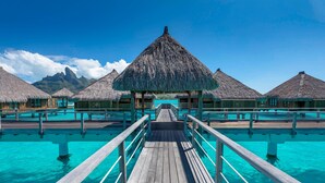 A wooden pier leading to overwater bungalows with thatched roofs, surrounded by clear turquoise water. - The St. Regis Bora Bora Resort (Bora Bora)