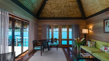 A room with a large window overlooking a body of water, a dining table with chairs, a sofa, and a TV.