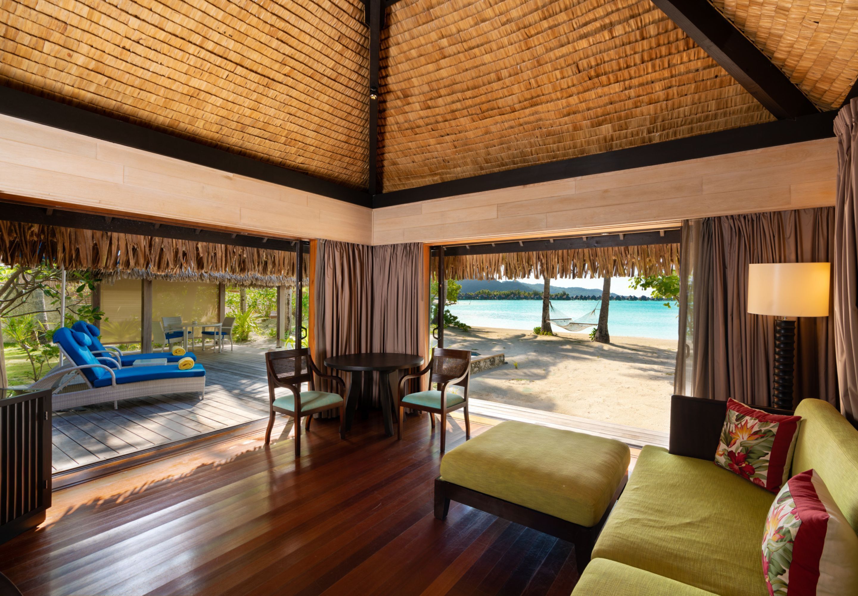 Una habitación con piso de madera, un sofá, una mesa con sillas y vista a la playa.