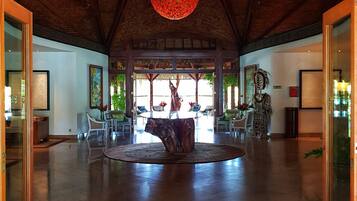 A spacious lobby with a central wooden table, a decorative ceiling light, and a large window offering a view of the outdoors.