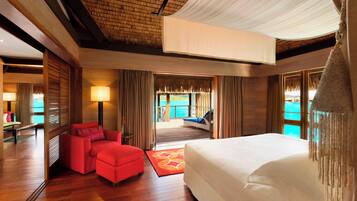 A hotel room with a large bed, a red sofa, a wooden floor, and a view of the sea through the window.