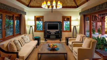 A living room with a sofa, armchairs, a coffee table with fruit, a TV, and decorative lamps.