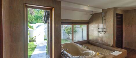 A modern bathroom with a large bathtub, a shower, and a view of a garden.
