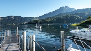 Una marina con barcos amarrados, un muelle que se adentra en aguas tranquilas y montañas al fondo.