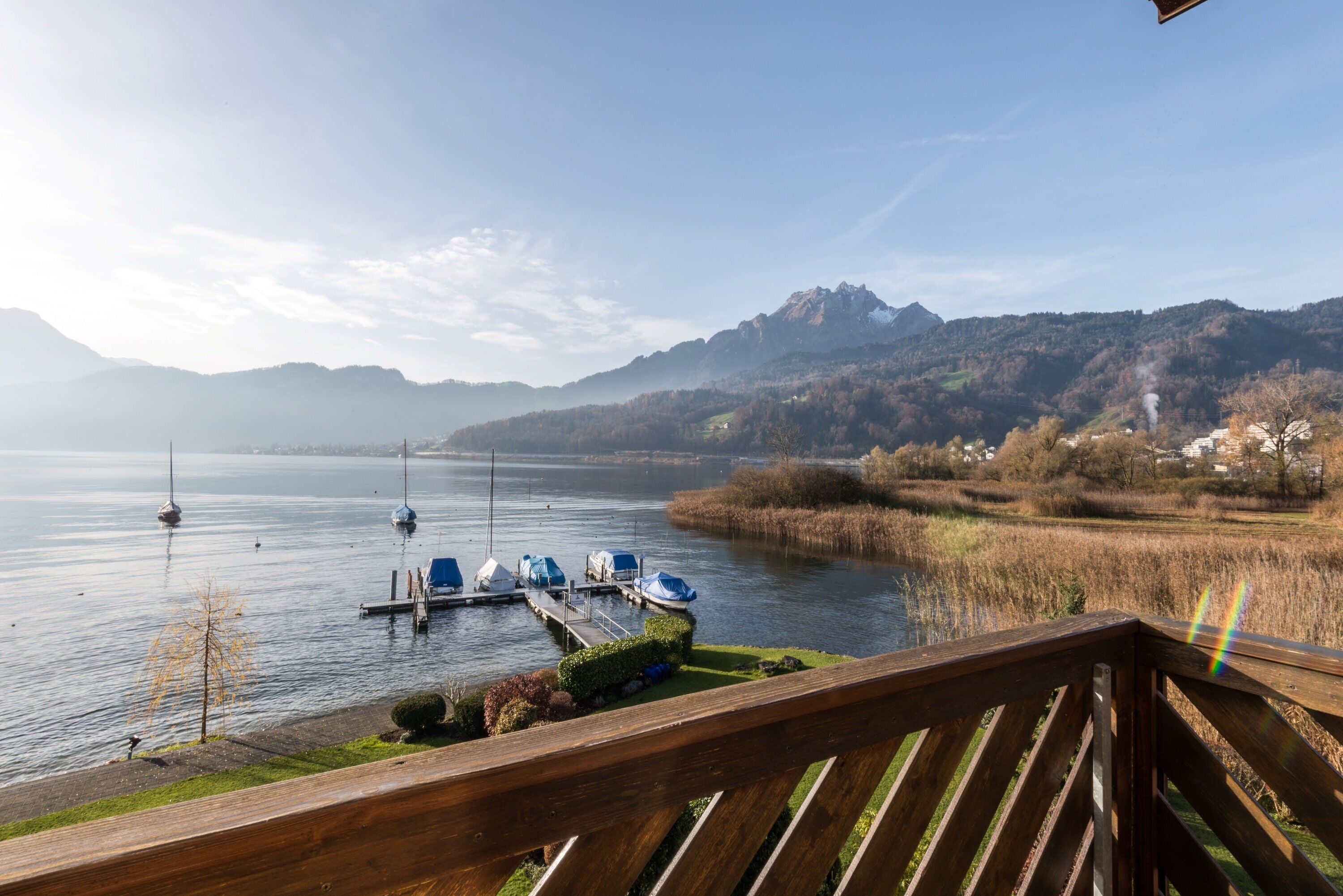 Une vue sur le lac, avec des bateaux amarrés, une terrasse en bois et des montagnes en arrière-plan.