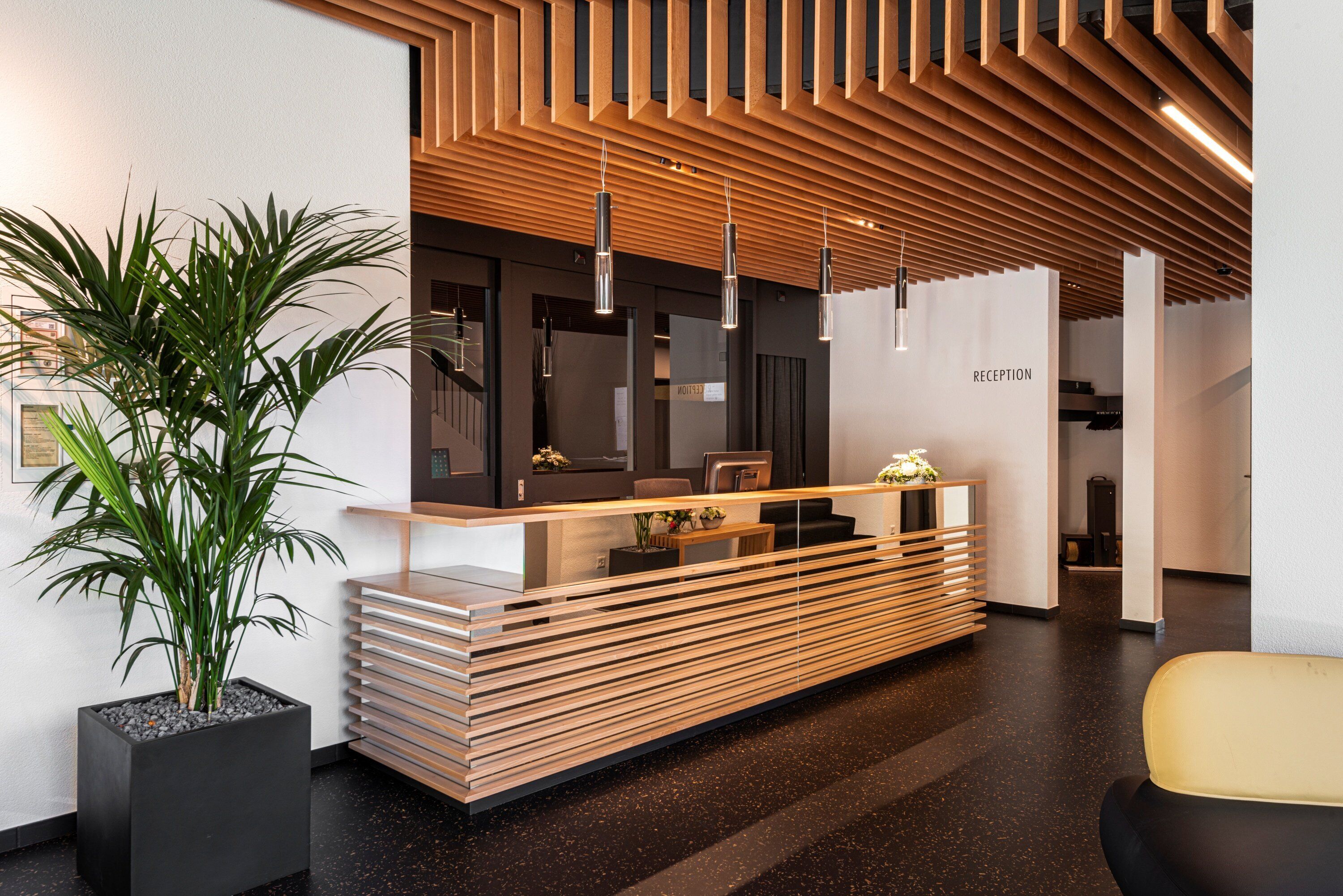 Un espace d’accueil au design moderne, comprenant un comptoir d’accueil, une plante en pot et un comptoir en bois à lattes.